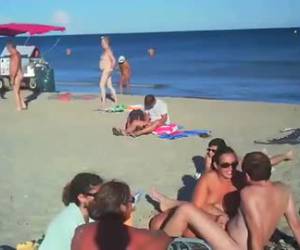 Tussen de mensen op het naakt strand, pijpt zijn vrouw zijn stijve lul en trekt hem af. 